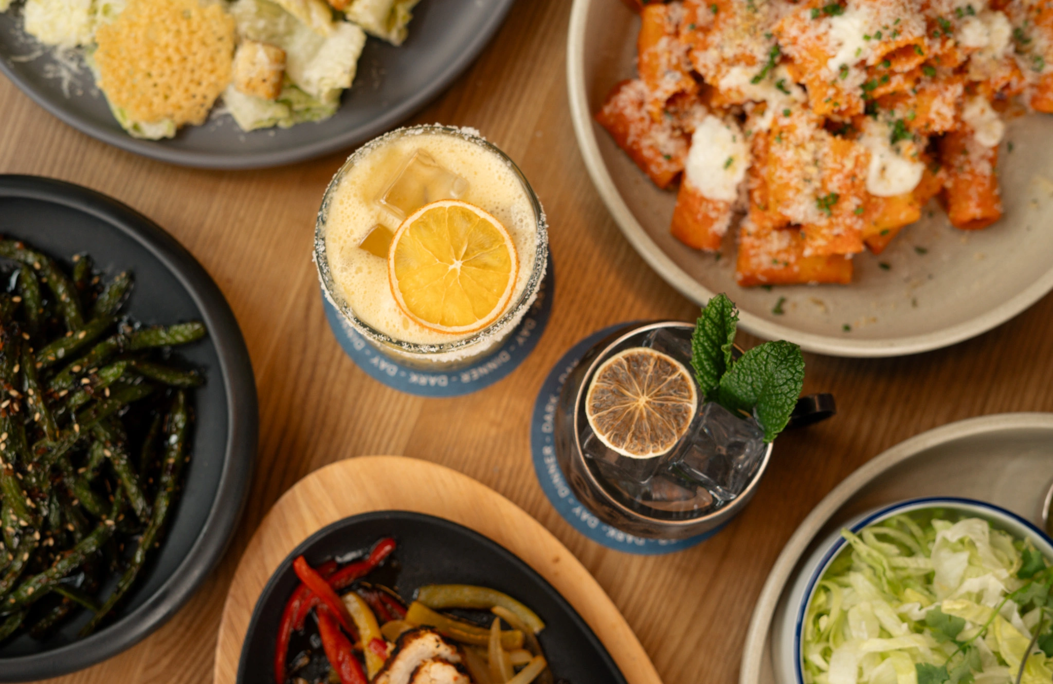 Ray's comfort food spread featuring cocktails, handmade pasta, fresh greens, salad, and share plates on a wooden dining table in Yaletown.