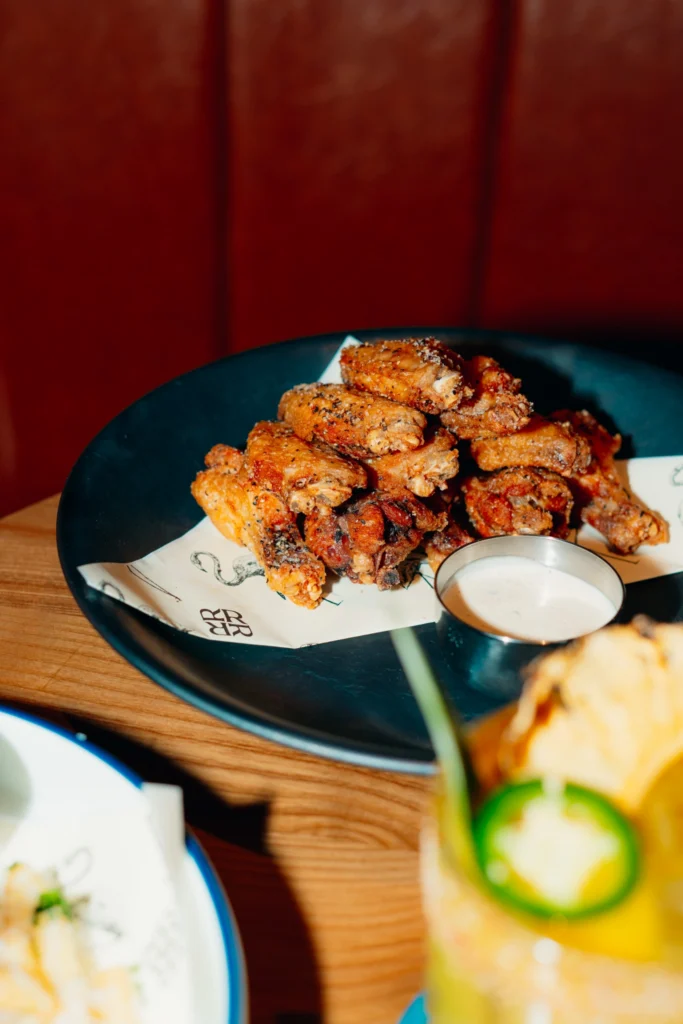 Ray's crispy hot chicken served with dipping sauce alongside colorful cocktails on a wooden table.