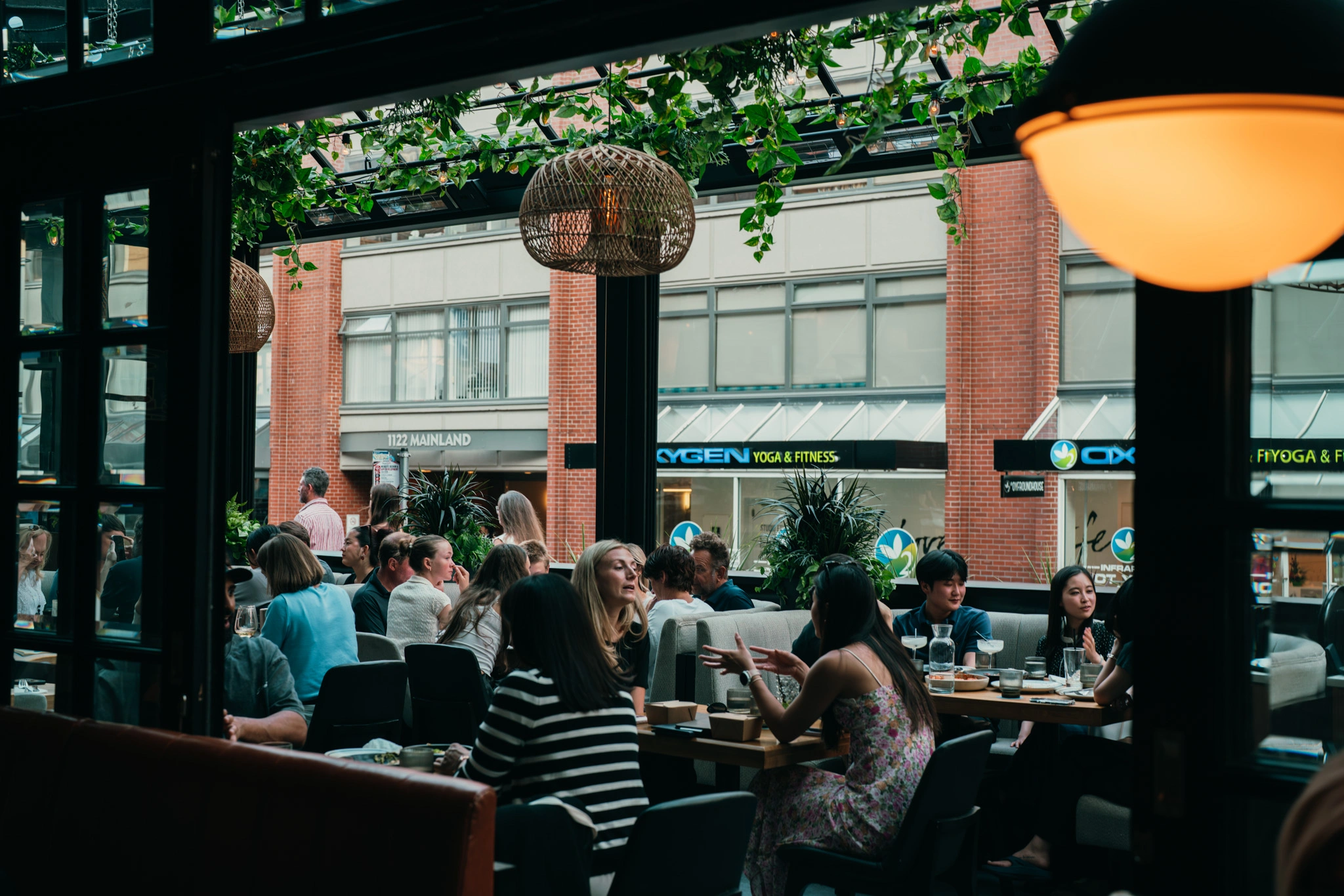 Busy café with customers seated at tables near large windows overlooking a brick street with storefronts