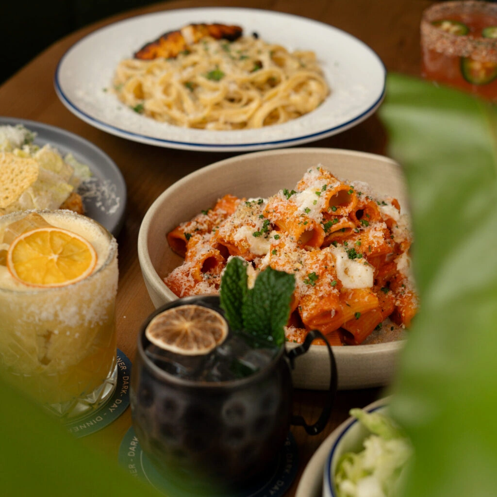 Overhead view of Cajun Chicken Alfredo, Spicy Vodka Rigatoni, cocktail on a wooden dining table.