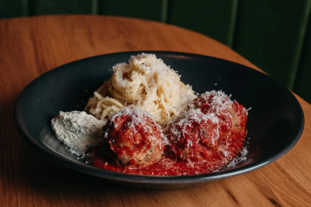 Artistic plated dessert with two red-coated balls, shredded noodles, and white mousse on black plate